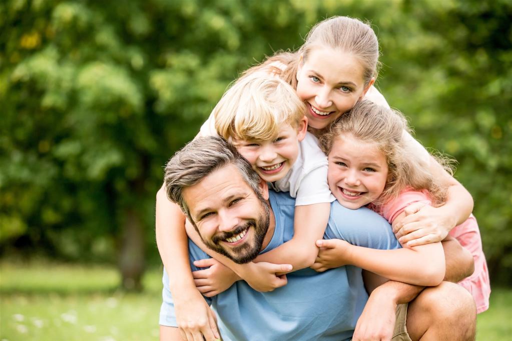 Lächelnde Familie mit zwei Kindern im Freien, die sich umarmen